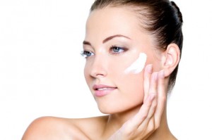 Beautiful woman applying moisturizer cosmetic cream on cheek - on a white