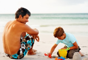 Happy father and son on a beach vacation, boy making sand castle